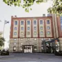 Suuri tiilirakennus, jossa modernit lasiosat ja sisäänkäynti. Liput ja puut kehystävät aurinkoista näkymää. MAGASINET, HAMNGATAN 9.