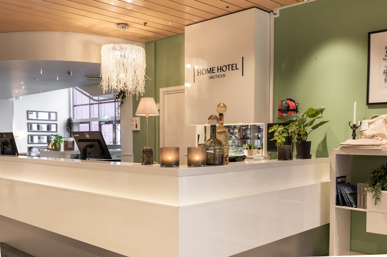 Kutsuva hotellin vastaanottotiski, jossa lukee HOME HOTEL ARCTICUS, valmiina vieraiden sisäänkirjautumiseen.