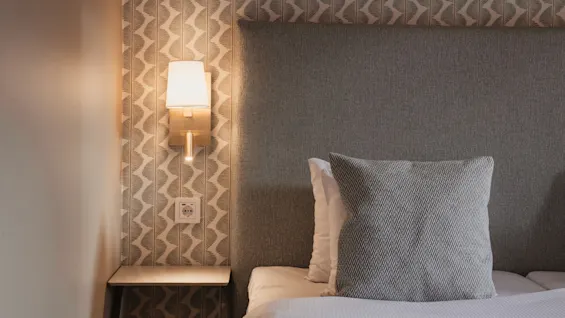 Et hyggeligt sengeområde på Home Hotel Wellington med en varm væglampe, mønstret tapet og en komfortabel seng.