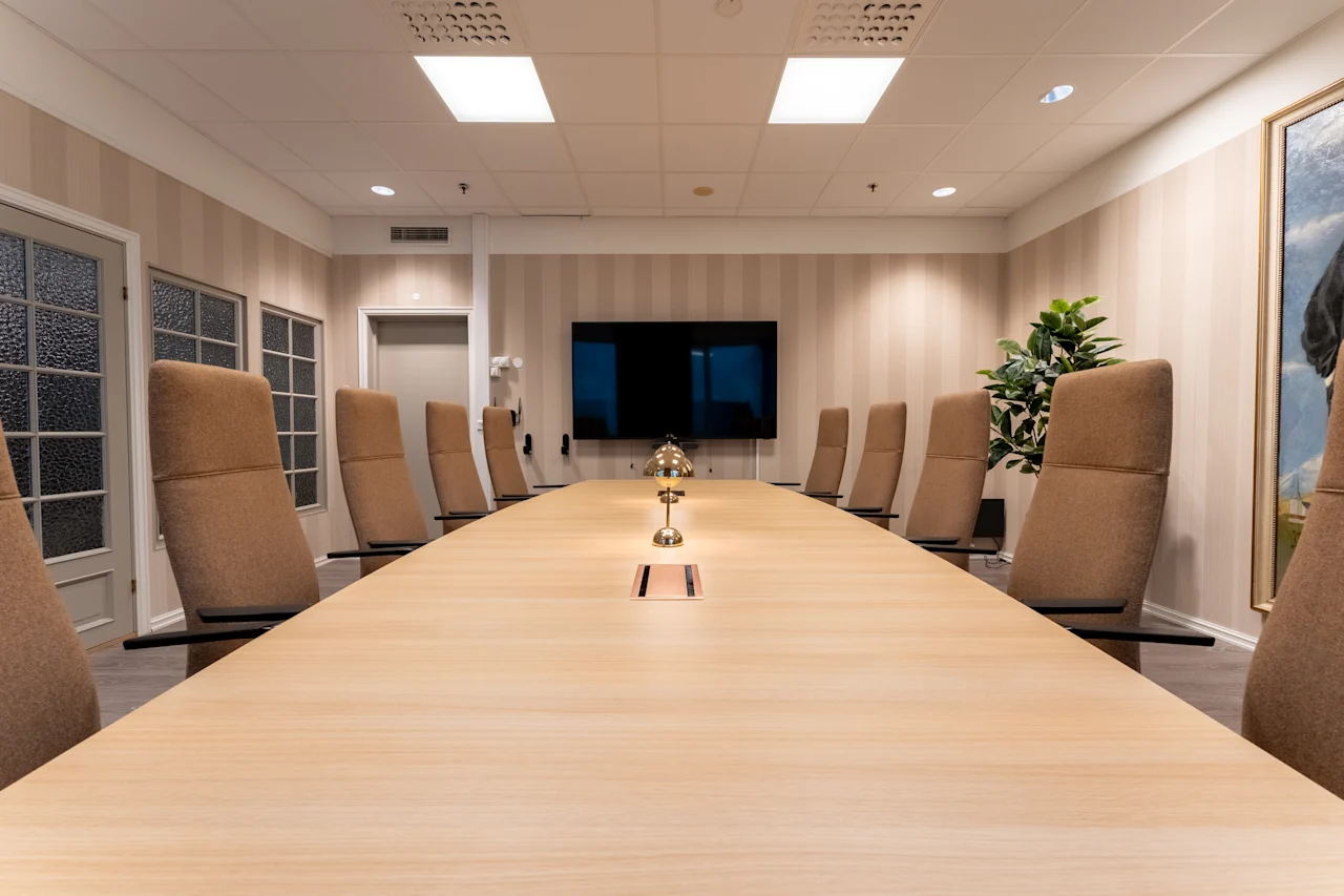Moderni kokoushuone, jossa on pitkä puupöytä, mukavat tuolit ja suuri näyttö, valmiina tuottavaan kokoukseen.