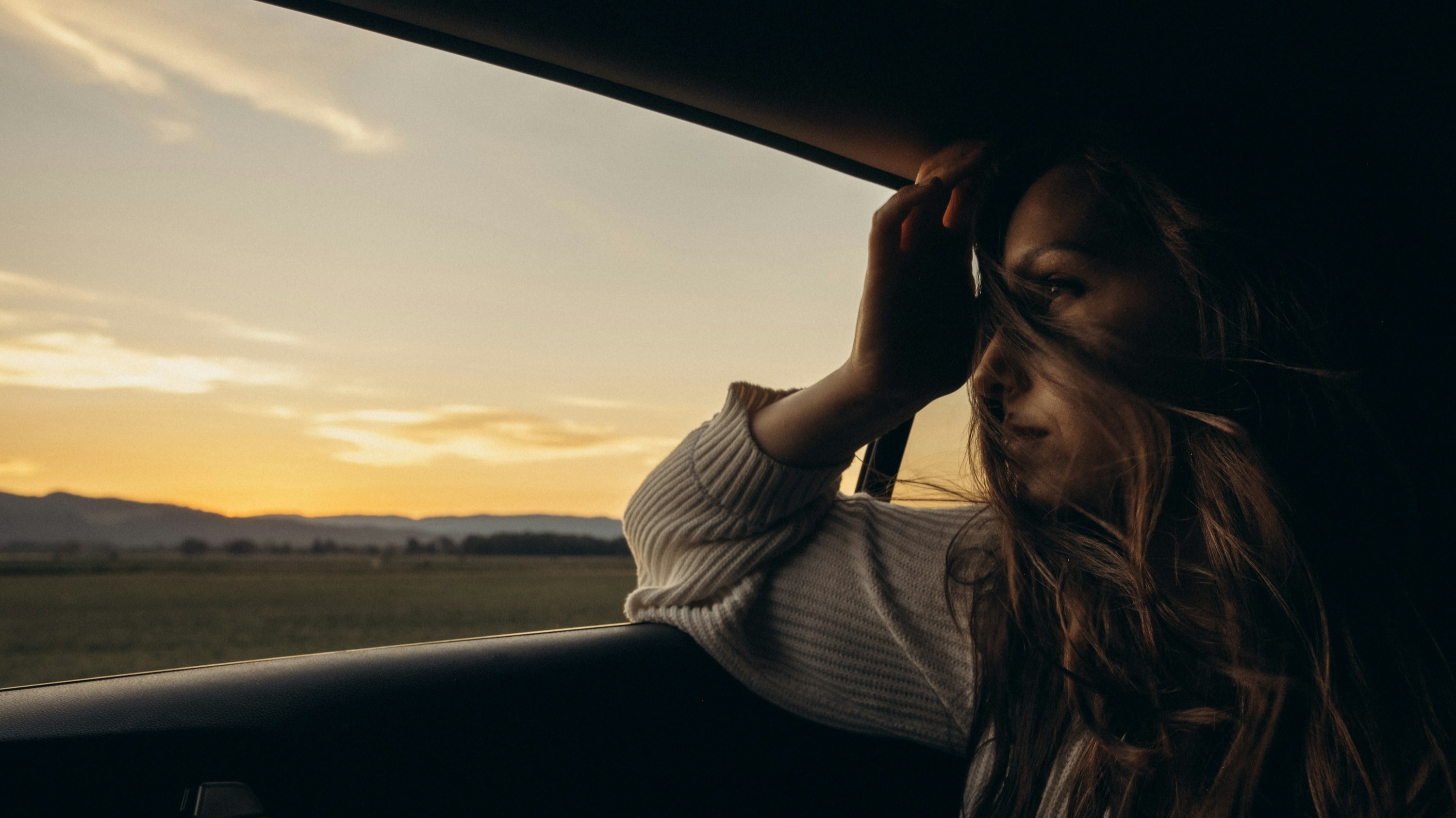 Njuter av en naturskön bilresa i solnedgången, med håret som blåser lätt i vinden.