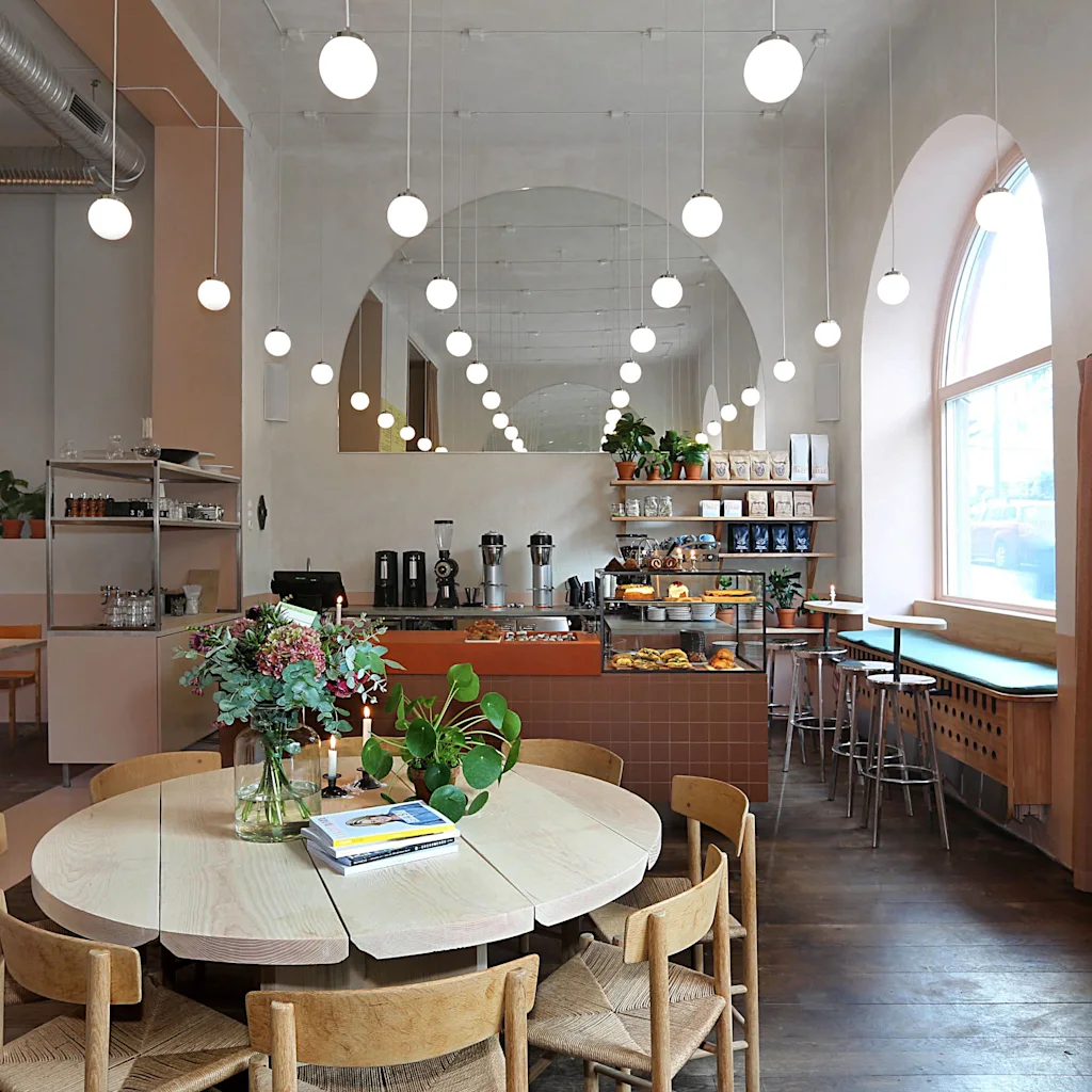 En moderne café med sfæriske lys, stort træbord og madudstilling. Menu: Noodle Salad og Tuna Sandwich.