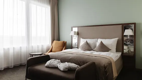 Ett mysigt hotellrum med en stor säng, en bekväm schäslong med badrockar och ett ljust fönster.