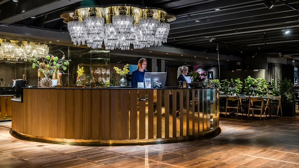 Ett hotellreceptionsdisk med personal under eleganta kristallkronor i en lyxig lobby.