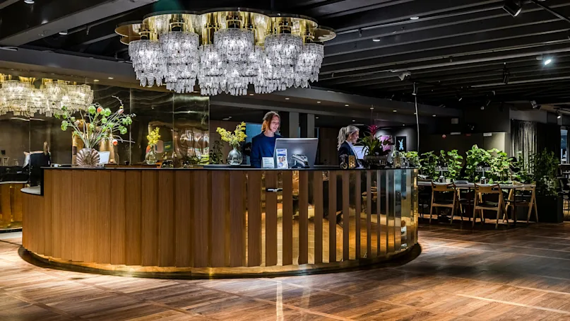 A hotel reception desk with staff, under elegant chandeliers, in a luxurious lobby.