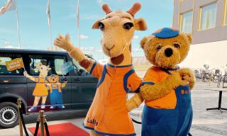 The Lollo & Bernie mascots standing outside next to a bus.