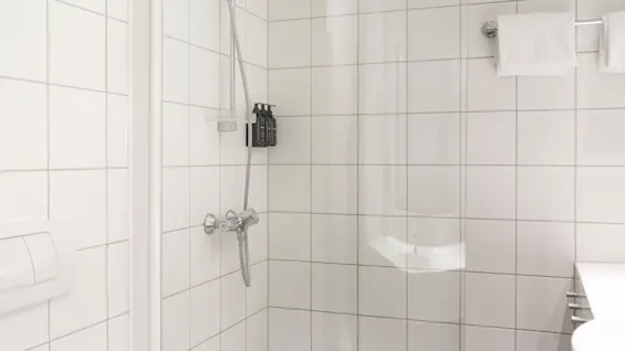 Et lyst og funksjonelt hotellbad med dusj, essensielle toalettartikler og friske håndklær, designet for gjestekomfort.