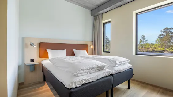 A bright hotel room with two comfortable beds and large windows offering a serene view of nature.