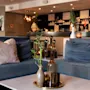 En hyggelig hotellounge med bløde blå sofaer, et sofabord prydet med bambus og glasflasker, og en smart bar.