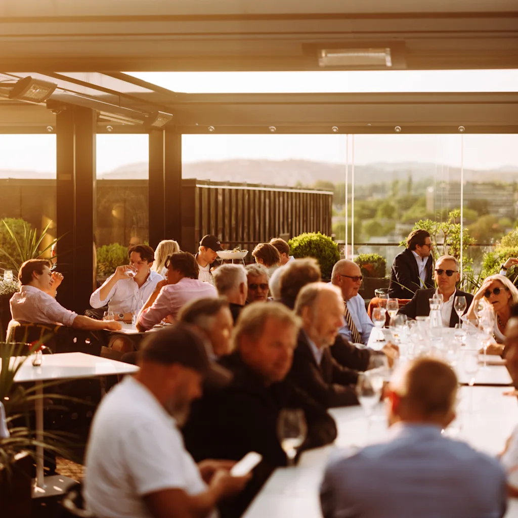 A group of people enjoying an outdoor gathering on a sunny rooftop terrace with a scenic view.