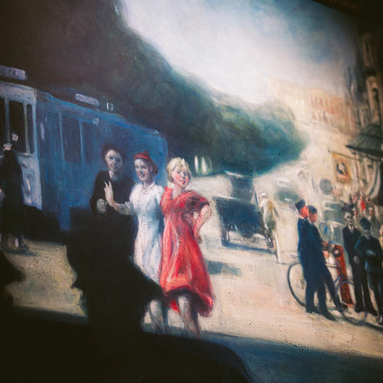 Three women in bright, vintage dresses walk confidently on a bustling street near an old blue tram, surrounded by people and historic buildings, capturing a lively urban scene.