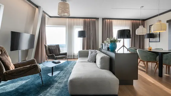 Large gray sofa facing a flat-screen TV in a modern living room. Nearby, a table with books, armchairs, and decorative lamps enhance the cozy atmosphere. Artwork reads: "Wonderful Copenhagen".