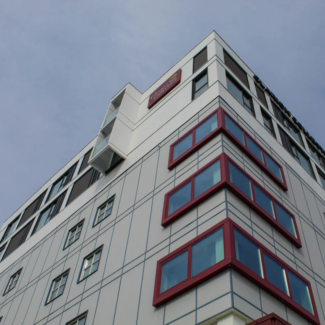 En høj, moderne bygning med rødrammede vinduer strækker sig mod en klar himmel.