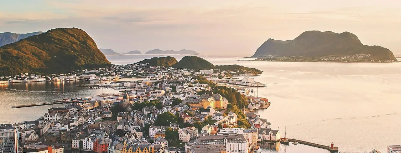 An aerial view of a picturesque coastal town with colorful buildings, surrounded by mountains and calm waters under a warm sky.