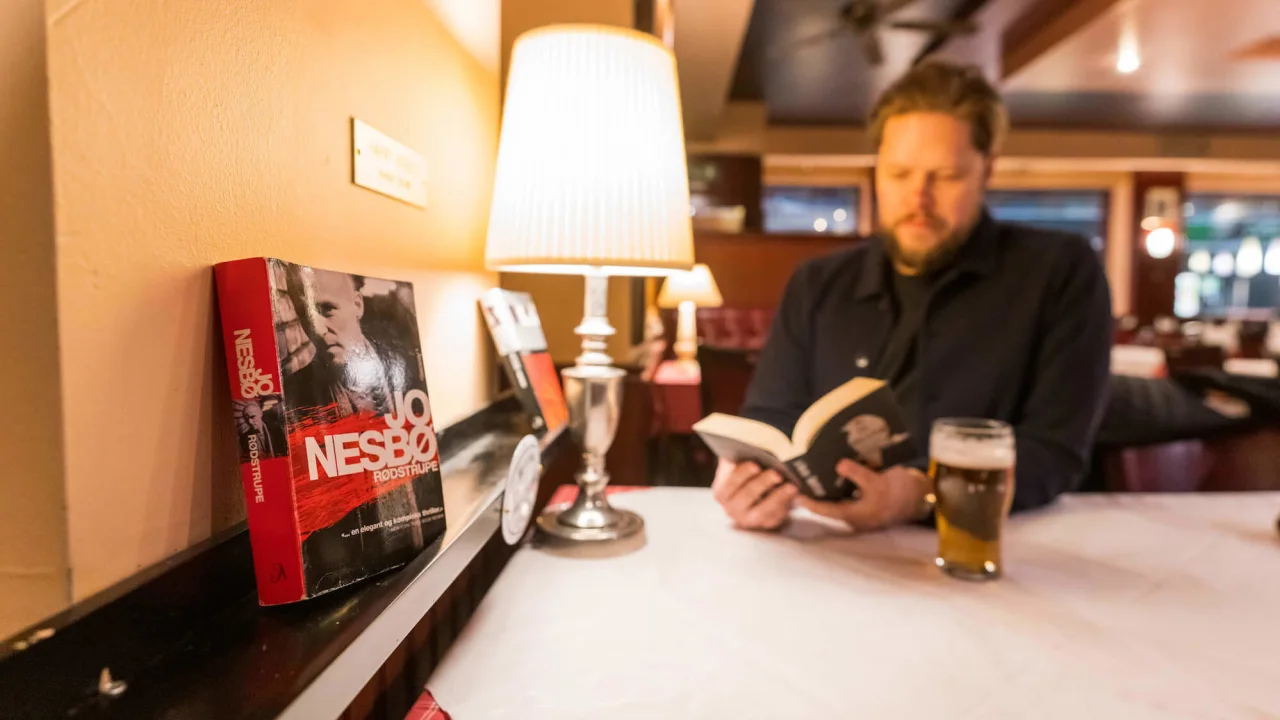 Man reading a book by Jo Nesbø at a bar.