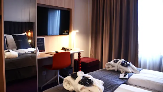 A neatly arranged hotel room with double bed, desk, and flat-screen TV in a modern decor.