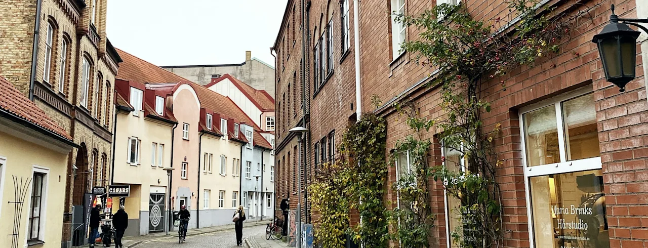 En sjarmerende brosteinsgate i Lund med folk som går og sykler forbi gamle bygninger. Synlig tekst: CIGARR, Harstudio, 046-15 20 40.