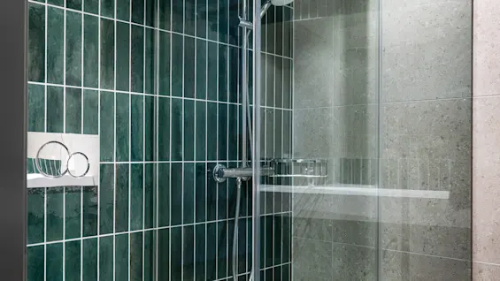 Et moderne bad med et hvitt toalett og en dusjkabinett i glass med mørkegrønne og grå flislagte vegger.