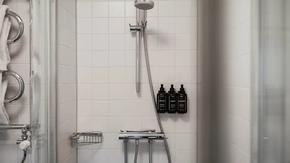 En ren, flisebelagt bruser på Home Hotel Wellington med flasker til body wash, shampoo og balsam, samt friske håndklæder.