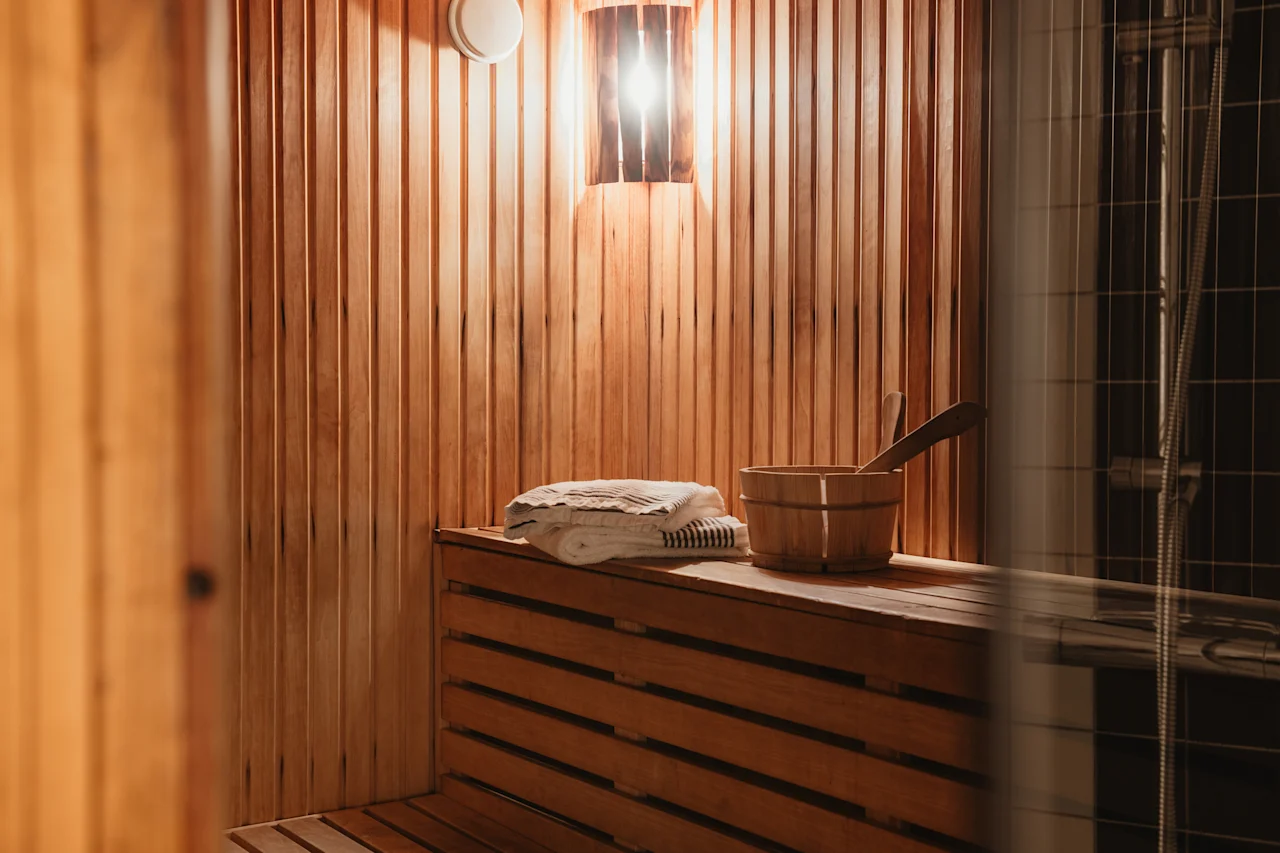 Home Hotel Kung Oscar sauna interior with warm wooden benches, towels, and a bucket, ready for relaxation.