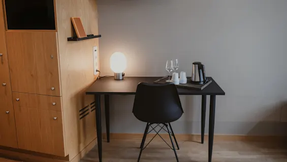 A cozy corner in a hotel room at Home Hotel Uppsala with a desk, chair, lamp, and coffee/tea setup, perfect for relaxation.