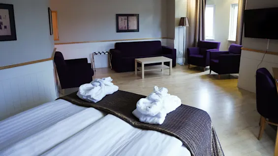 A neat hotel room with twin beds, towels shaped like swans, a sofa set, and a flat-screen TV.