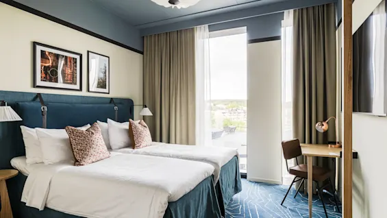 Et moderne hotelværelse på Hernö Gin Hotel med to komfortable senge, et skrivebord og et stort vindue med udsigt.