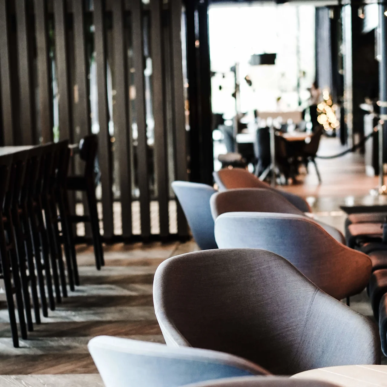 Buede, moderne stoler står pent oppstilt ved siden av bord i en stilig, svakt opplyst kafé. Parkettgulv og en panelvegg tilfører varme til det moderne interiøret.