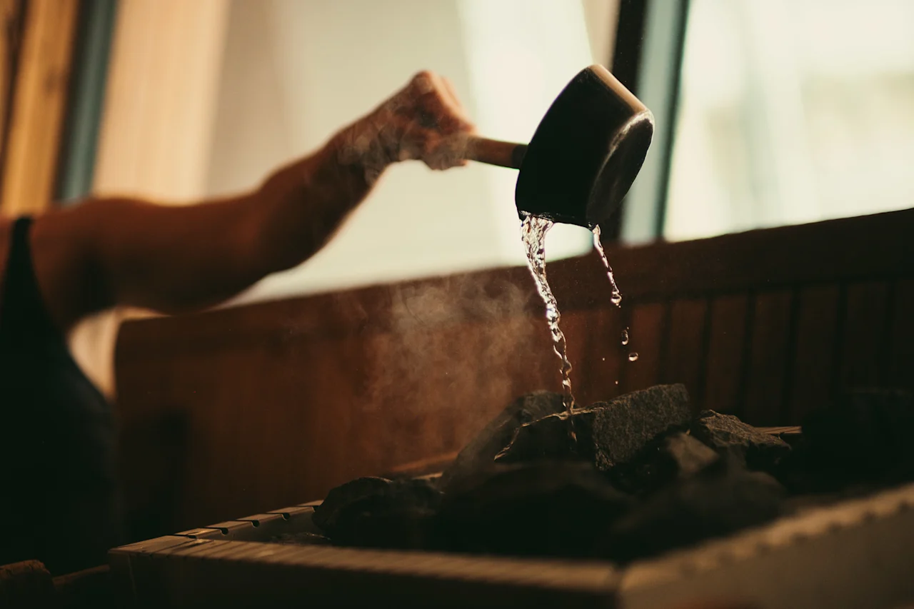 En person hælder vand på varme saunasten, hvilket skaber damp til en afslappende oplevelse.
