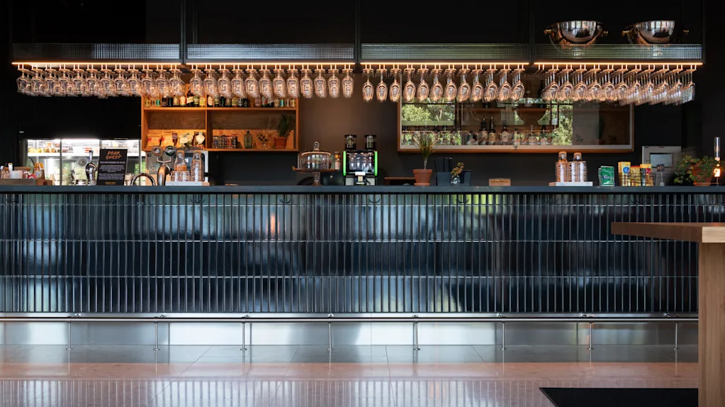 A sleek bar with hanging glasses, beverage taps, and a display of bottles set against a dark backdrop in a modern interior.