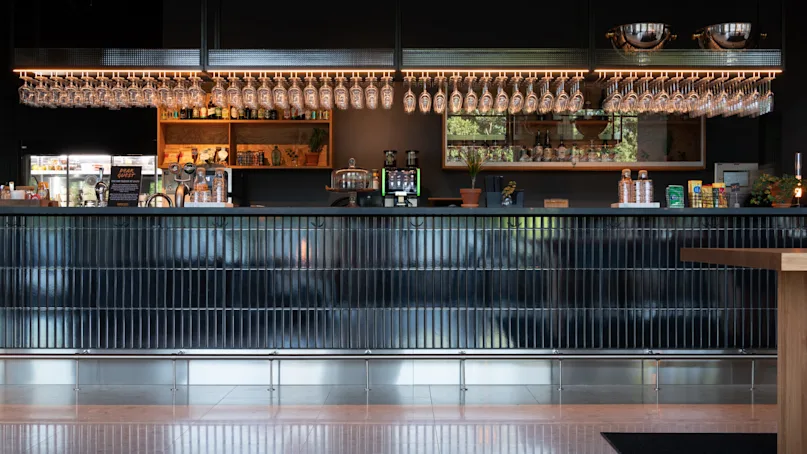 A sleek bar with hanging glasses, beverage taps, and a display of bottles set against a dark backdrop in a modern interior.