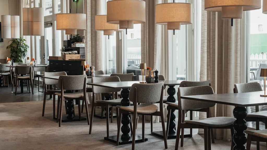 Et moderne og indbydende restaurantinteriør med komfortable siddepladser, elegant belysning og store vinduer, der giver naturligt lys.