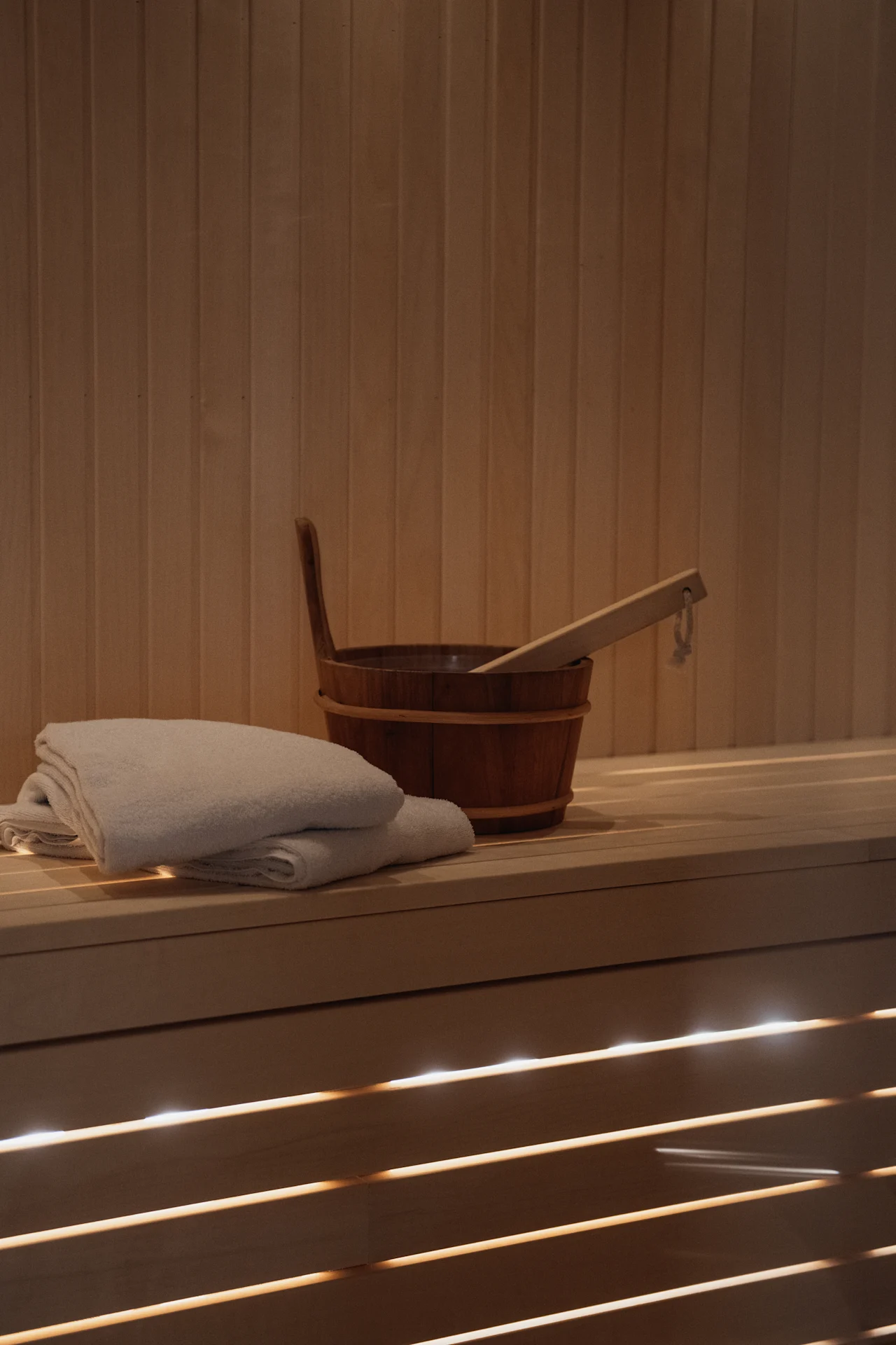 En mysig bastuinteriör med träbänkar, en hink, skopa och fräscha handdukar, redo för avkoppling.