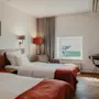Viihtyisä hotellihuone, jossa kaksi erillistä sänkyä, työpöytä ja ikkuna, josta näkyy teollisuusalue.