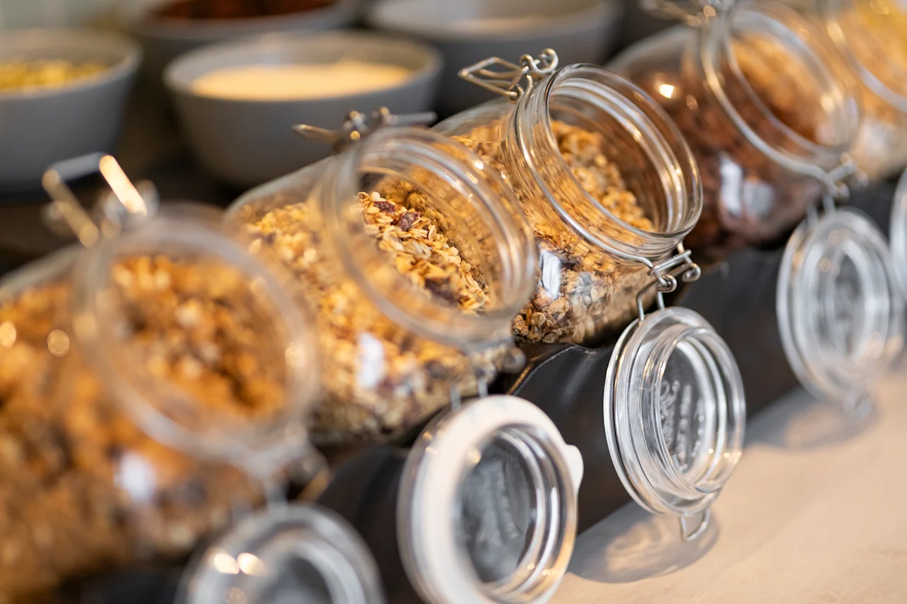 A close-up of glass jars filled with granola and cereal, ready for self-service at a breakfast buffet.
