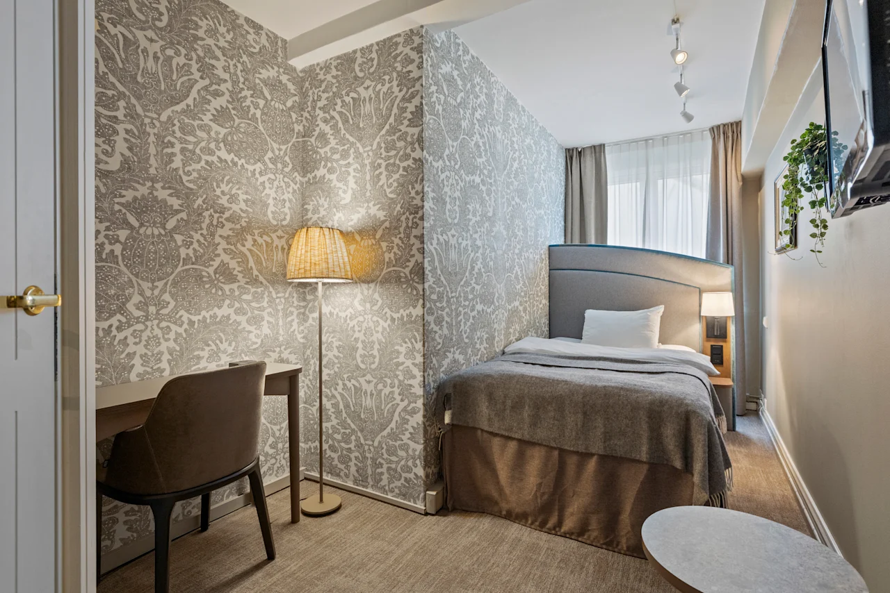 A welcoming hotel room featuring a comfortable bed, a functional desk area, and soft lighting, with decorative wallpaper.
