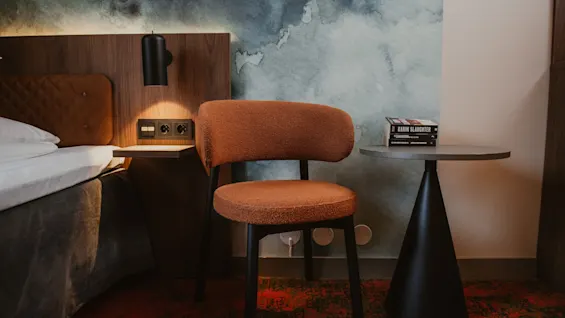 Et koselig hotellrom med en seng, en komfortabel stol og et sidebord med bøker, inkludert en av Karin Slaughter.