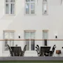 Utomhus sittplats med flera bord och stolar, placerade på en terrass. Omgiven av vita byggnadsväggar med fönster. Lugn atmosfär.