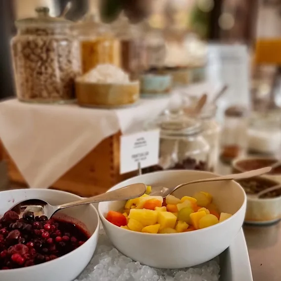 En fräsch frukostbuffé med skålar med bär och fruktsallad på is, samt burkar med flingor och havregryn.
