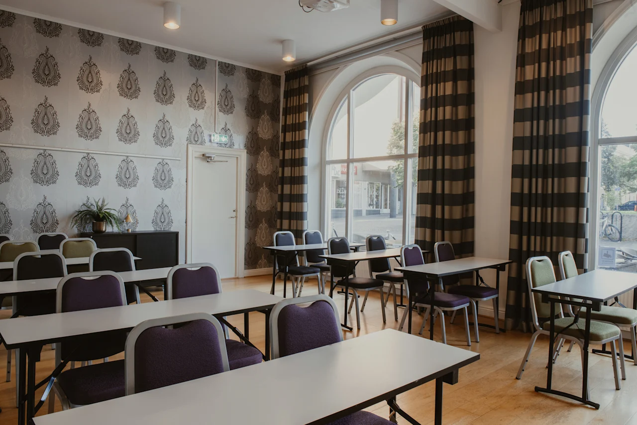 Ett mötesrum med bord, stolar, stora fönster och mönstrade väggar. En EXIT-skylt ovanför dörren, redo för konferens.