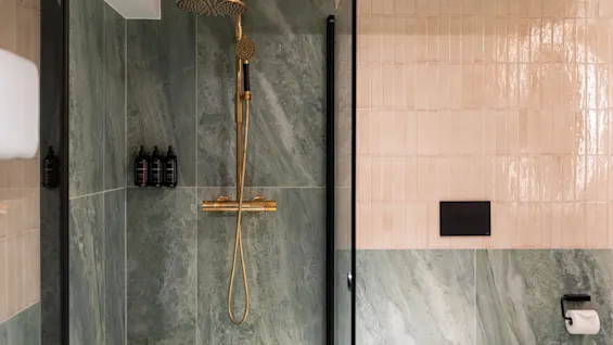 Et moderne bad med grønne marmormønstrede fliser og gullfargede dusjarmaturer, med toalettartikler og et toalettområde.