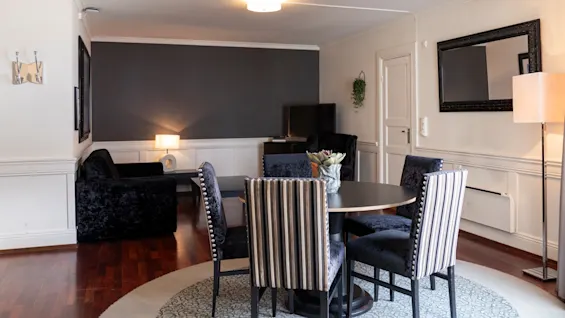 Et hyggeligt stue- og spiseområde med et rundt bord, komfortable stole, en sofa og et fjernsyn, med moderne design.