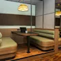 Cozy booth seating with a wooden table hosts a laptop and a mug in a warmly lit workspace. Modern pendant lighting and plush benches enhance the intimate office setting.