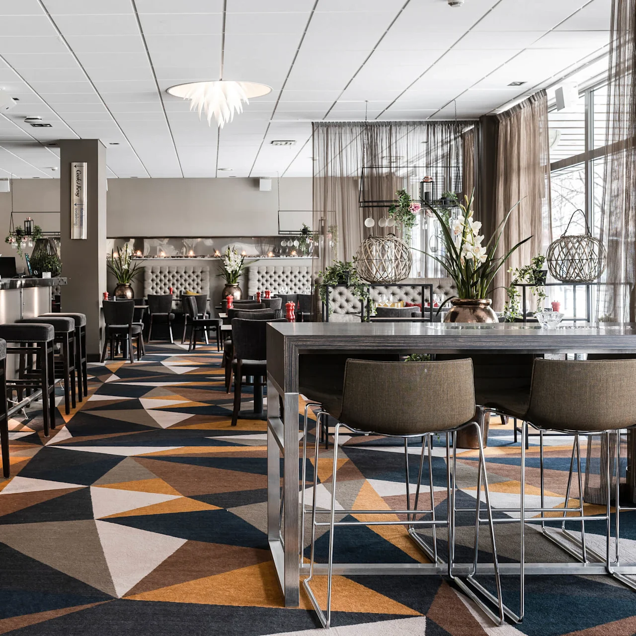 Bar med pallar och drycker, belägen i en modern restaurang med geometrisk matta. Text: "invit".