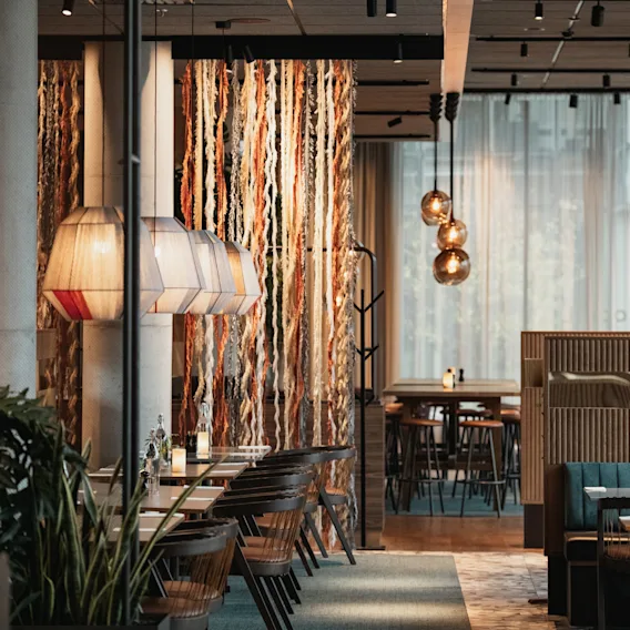 Modern hotellrestaurang med träbord, stilrena pendellampor och dekorativt hängande garn.