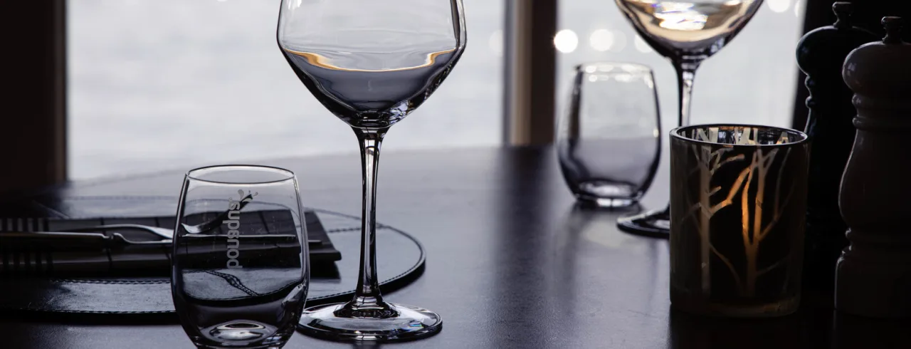 Empty wine glasses on a table, silhouetted against a bright window, implying a dining setting.