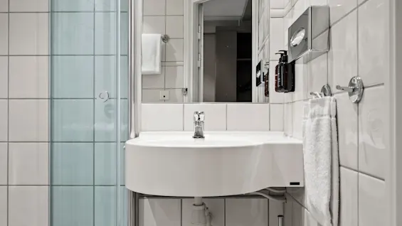 A bright and functional bathroom featuring white tiled walls, a glass-enclosed shower, and a sleek sink with a large mirror.