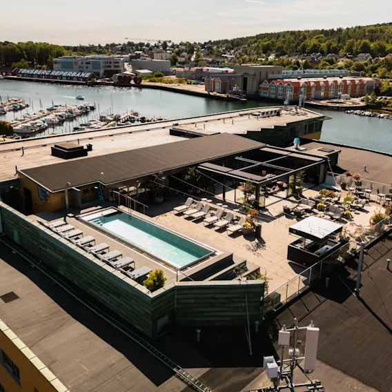 Takbasseng og salongområde med solsenger og uteservering, med utsikt over en havn med båter og en by.