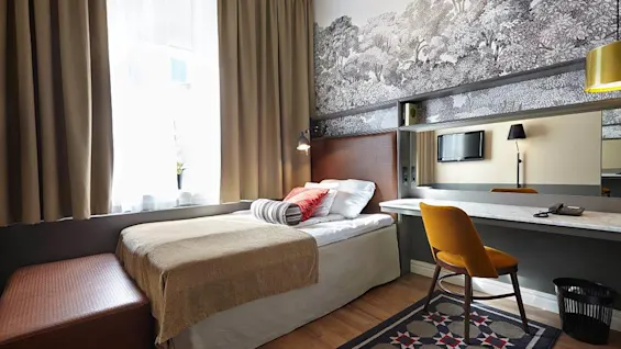 A cozy hotel room with a single bed, stylish desk area, and patterned wallpaper, showcasing a modern and comfortable design.