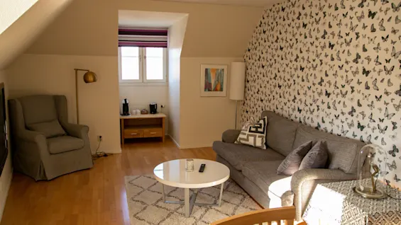 Cozy hotel room living area featuring a gray sofa, armchair, and butterfly patterned wallpaper.